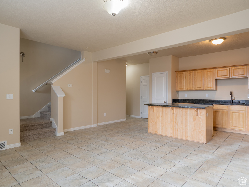 Kitchen featuring light brown cabinets, a kitchen island, baseboards, a breakfast bar, and a sink