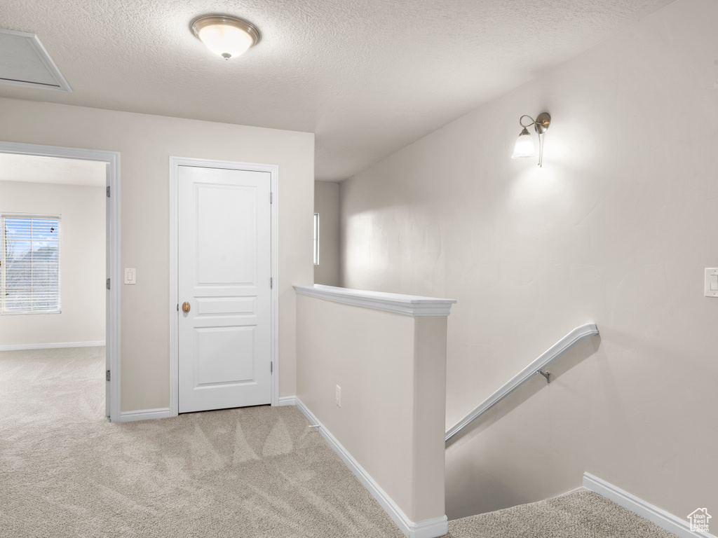 Hall featuring baseboards, an upstairs landing, carpet, and a textured ceiling
