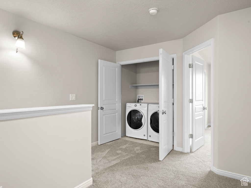 Clothes washing area featuring washer and clothes dryer, light carpet, a textured ceiling, laundry area, and baseboards