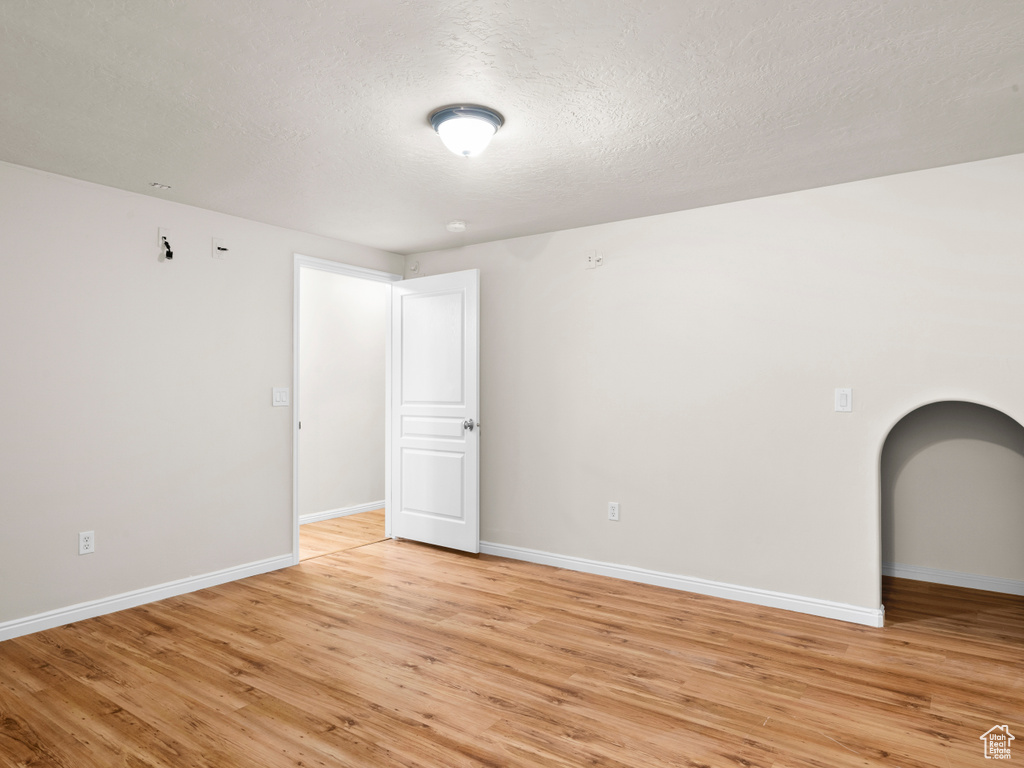 Spare room with baseboards, a textured ceiling, and light wood-type flooring