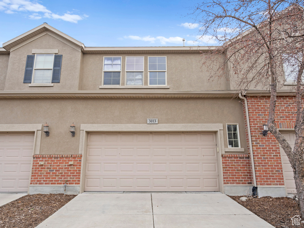 Exterior space with stucco siding, a garage, brick siding, and concrete driveway