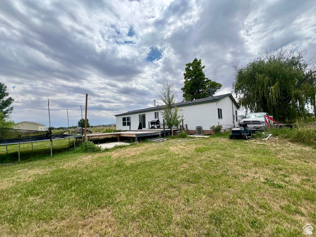 Back of house with a yard, a deck, central AC unit, and a trampoline