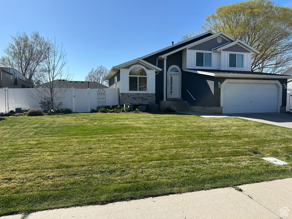 View of front of property featuring driveway, a front lawn, fence, and an attached garage