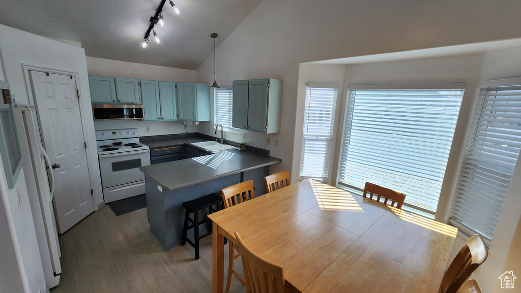 Kitchen featuring lofted ceiling, a peninsula, wood finished floors, white appliances, and a sink