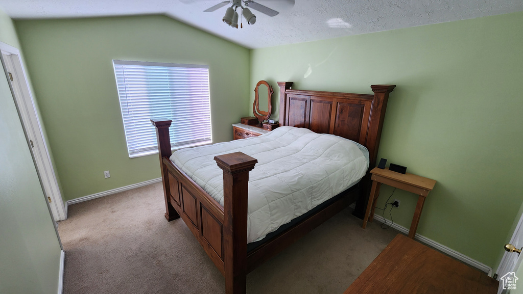 Bedroom featuring a ceiling fan, baseboards, vaulted ceiling, a textured ceiling, and light carpet