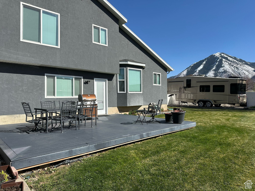 Back of property with stucco siding, a deck with mountain view, outdoor dining space, and a yard