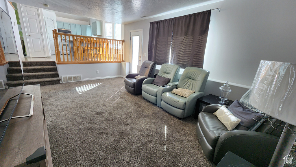 Carpeted living room featuring visible vents, baseboards, a textured ceiling, and stairs