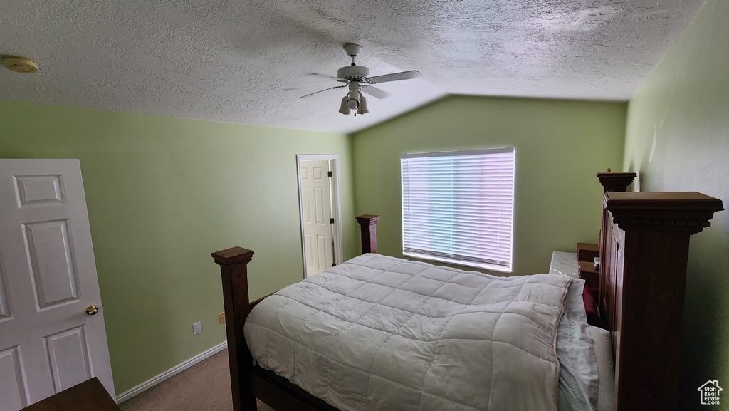 Carpeted bedroom featuring baseboards, a textured ceiling, a ceiling fan, and vaulted ceiling