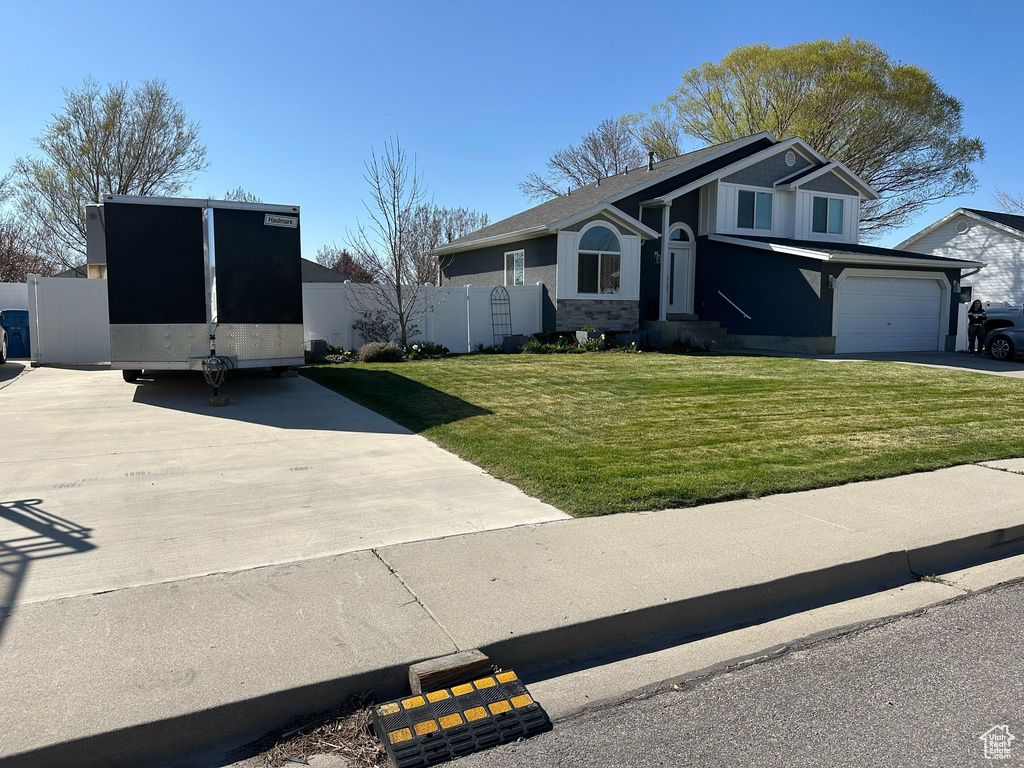 View of front facade with driveway, stucco siding, fence, and a front yard