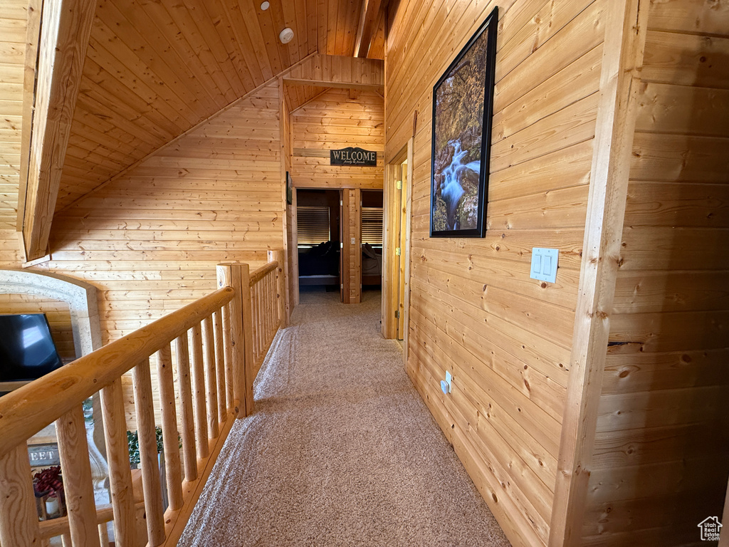 Hallway with wood walls, wood ceiling, vaulted ceiling, light colored carpet, and an upstairs landing