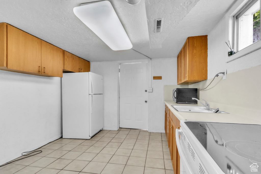 Kitchen with white appliances, a sink, a textured ceiling, light countertops, and light tile patterned floors