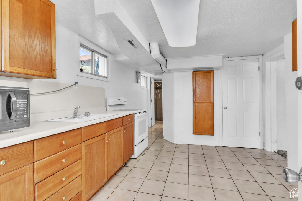 Kitchen with electric range, black microwave, light countertops, a sink, and light tile patterned flooring