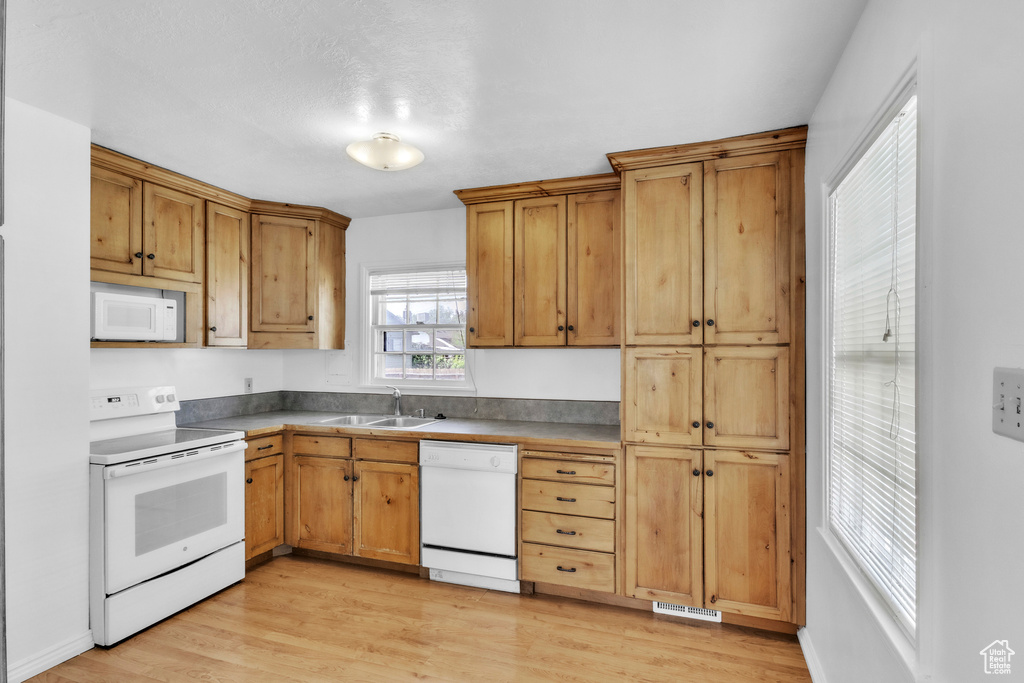 Kitchen featuring white appliances, a sink, light wood-type flooring, and brown cabinetry