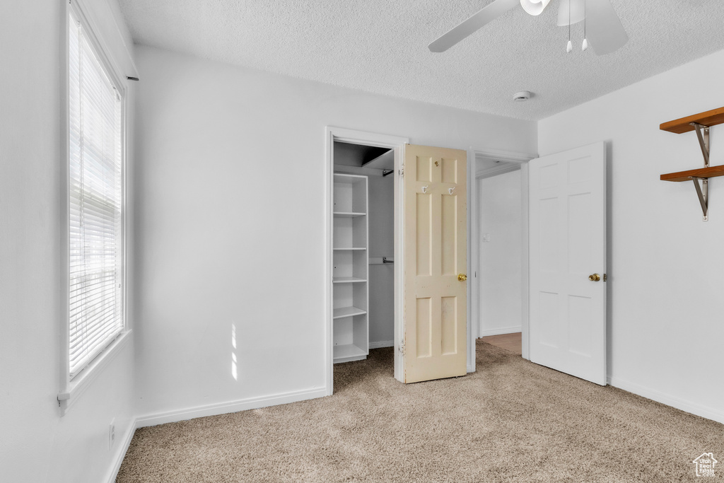 Unfurnished bedroom featuring carpet, a walk in closet, a textured ceiling, baseboards, and a ceiling fan