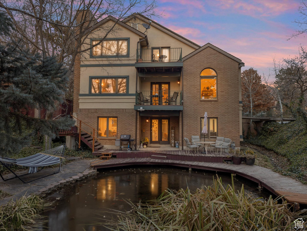 Rear view of house with stucco siding, a balcony, brick siding, and french doors