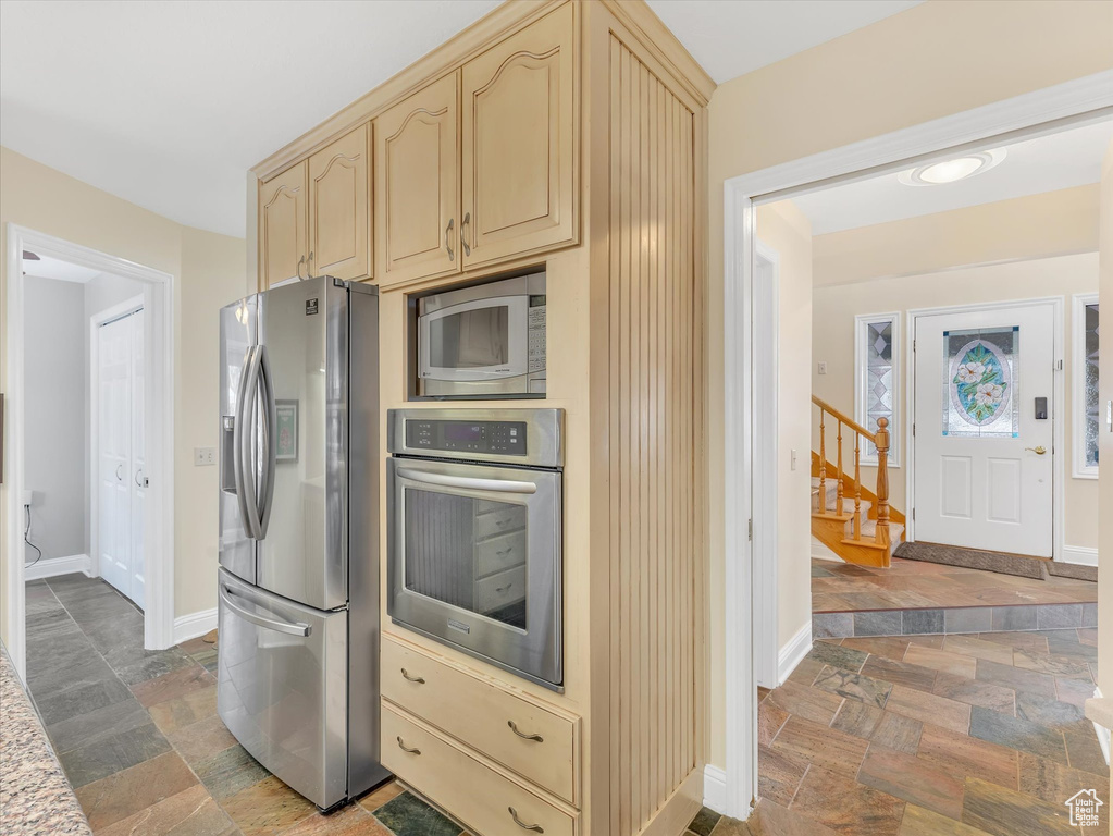 Kitchen featuring light brown cabinetry, stone finish floor, stainless steel appliances, and baseboards