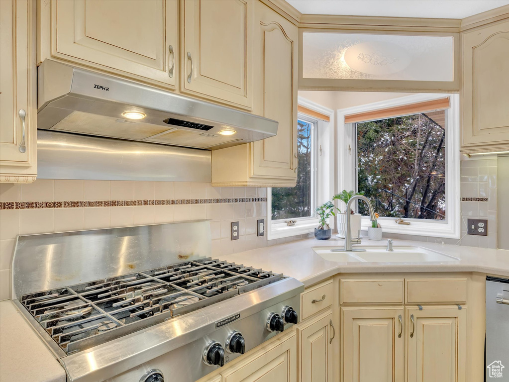 Kitchen with under cabinet range hood, a sink, cream cabinets, stainless steel appliances, and light countertops