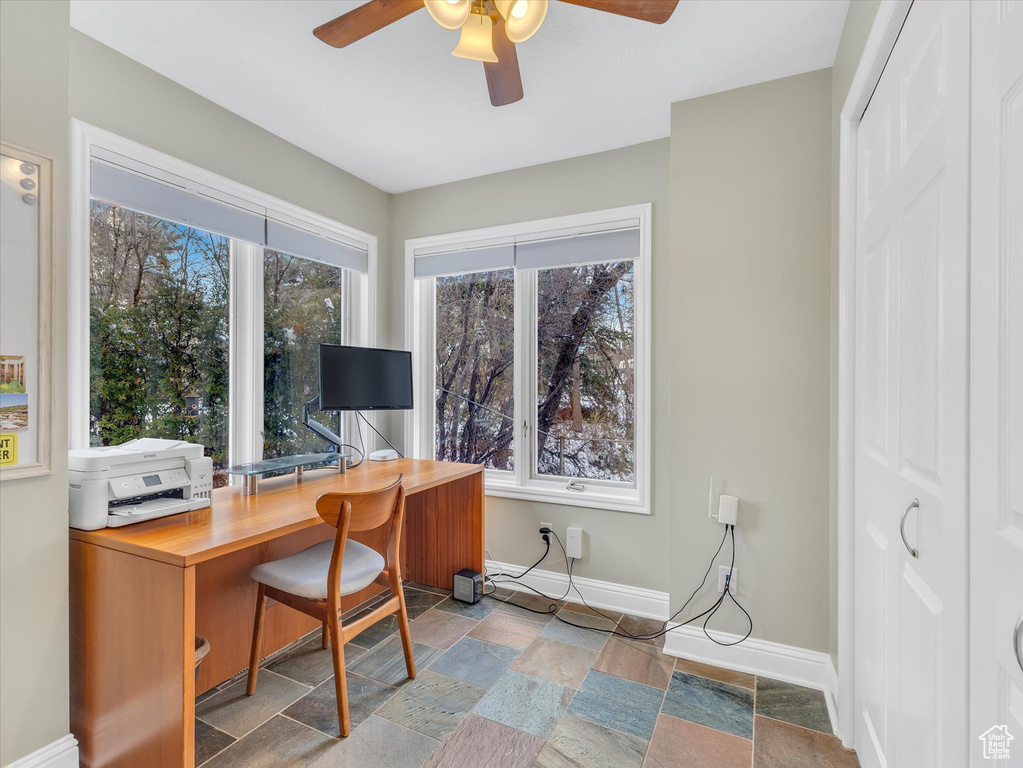 Office area featuring baseboards, stone tile flooring, and a ceiling fan