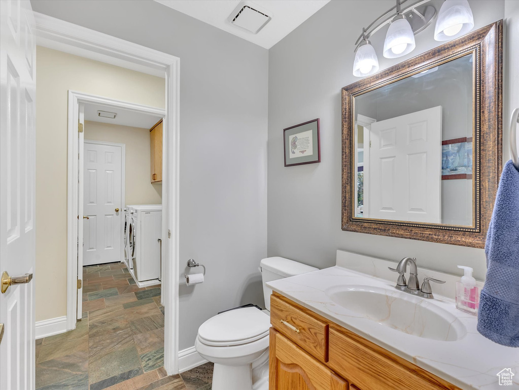 Bathroom with washing machine and clothes dryer, toilet, stone finish flooring, and baseboards