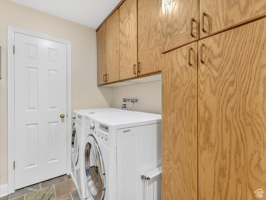 Clothes washing area with washer and dryer, cabinet space, and stone finish floor