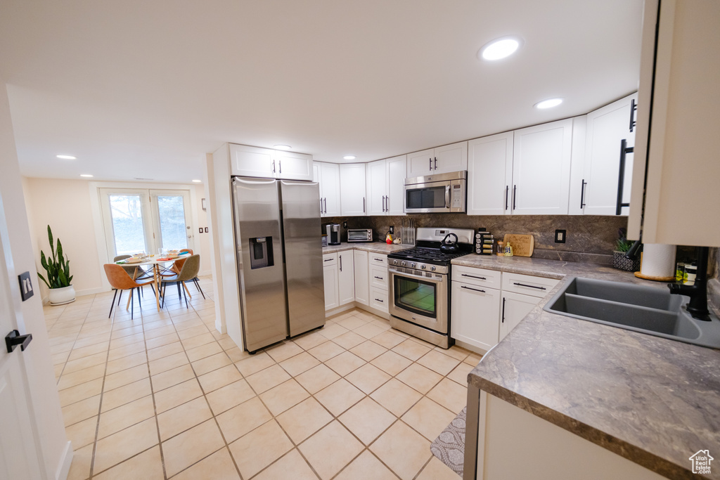 Kitchen featuring backsplash, light tile patterned floors, white cabinets, stainless steel appliances, and a sink