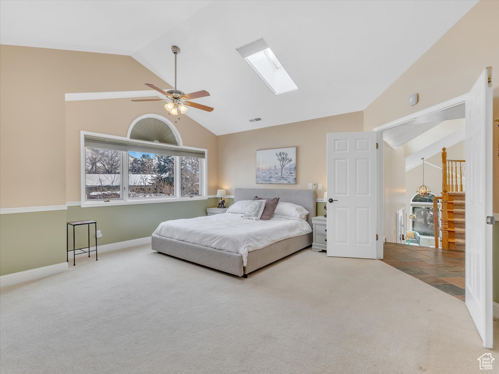 Carpeted bedroom with baseboards, lofted ceiling with skylight, visible vents, and ceiling fan
