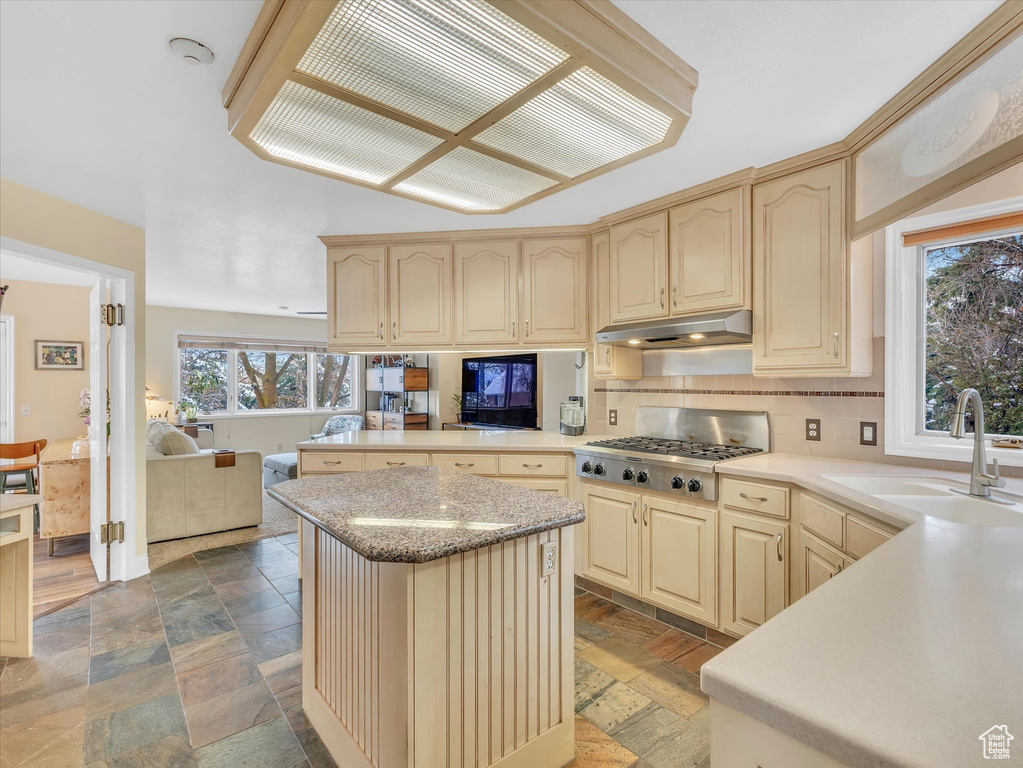 Kitchen with stone tile floors, stainless steel gas cooktop, a sink, under cabinet range hood, and open floor plan