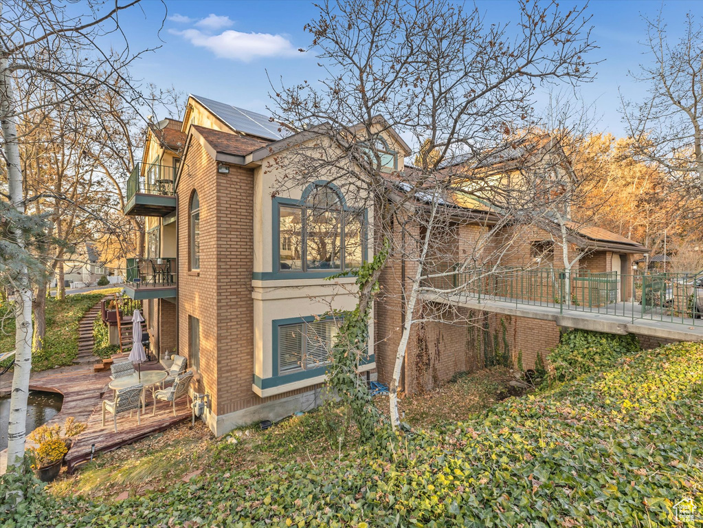 View of side of property featuring stucco siding, roof mounted solar panels, a balcony, brick siding, and stairs