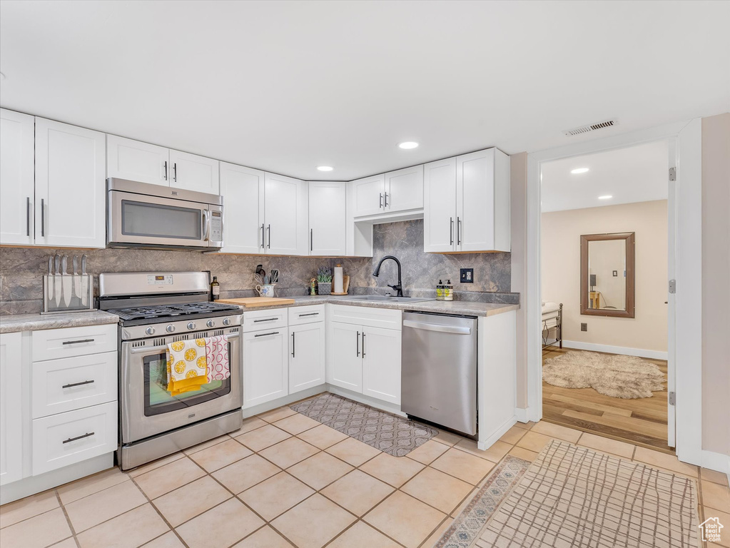 Kitchen featuring tasteful backsplash, visible vents, light countertops, white cabinets, and stainless steel appliances