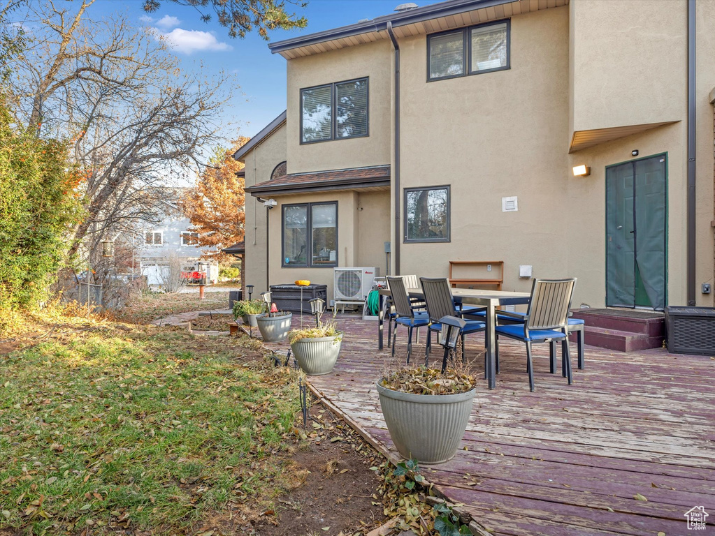 Rear view of property featuring outdoor dining space, stucco siding, a wooden deck, and ac unit
