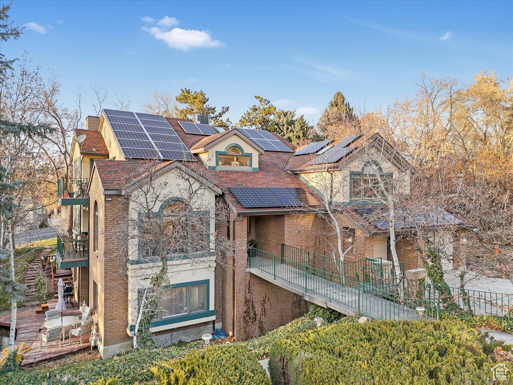 View of front facade with brick siding, fence, roof mounted solar panels, a chimney, and a balcony