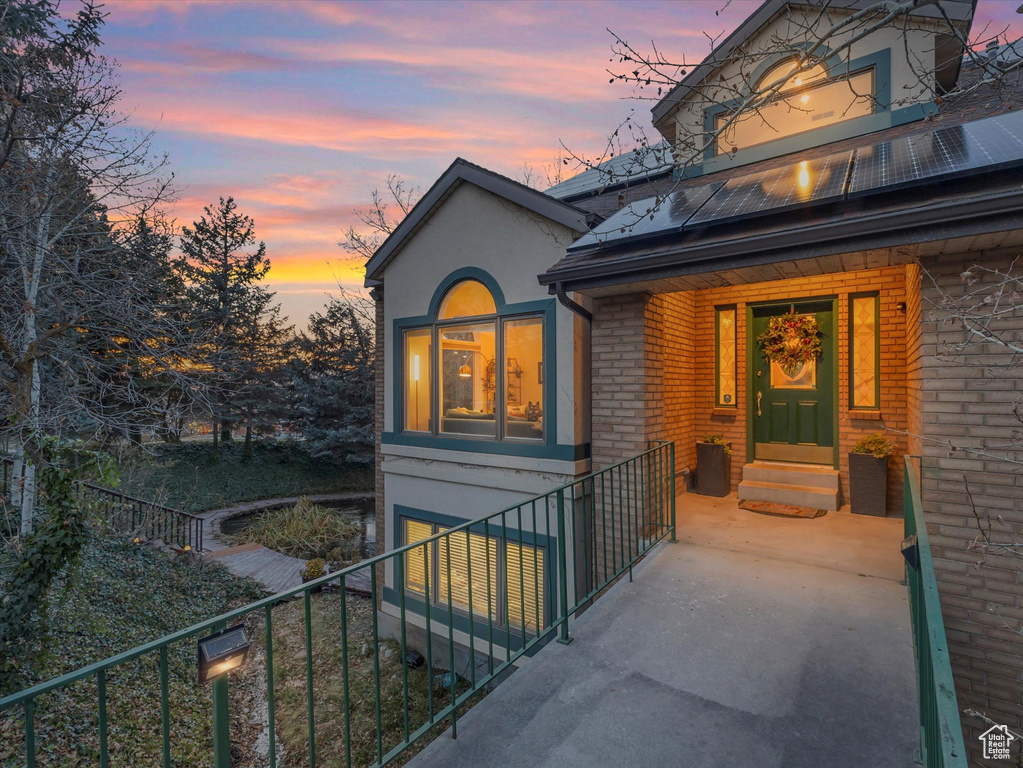 Exterior entry at dusk featuring stucco siding, brick siding, solar panels, and fence