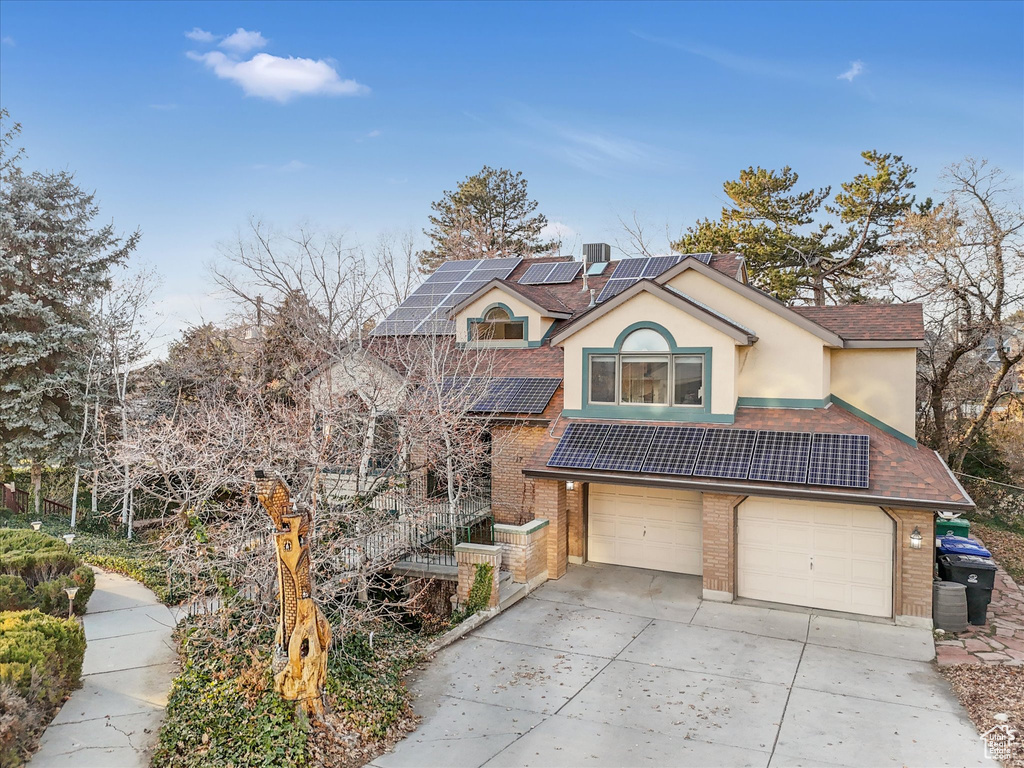 View of front of home featuring stucco siding, driveway, an attached garage, brick siding, and solar panels