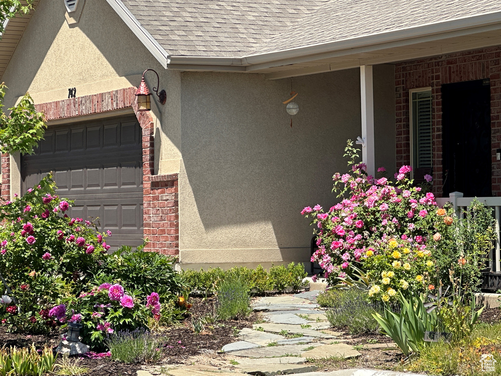 View of side of home featuring roof with shingles, stucco siding, an attached garage, and brick siding