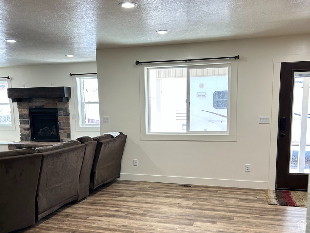 Living room with a stone fireplace, wood finished floors, baseboards, and a textured ceiling