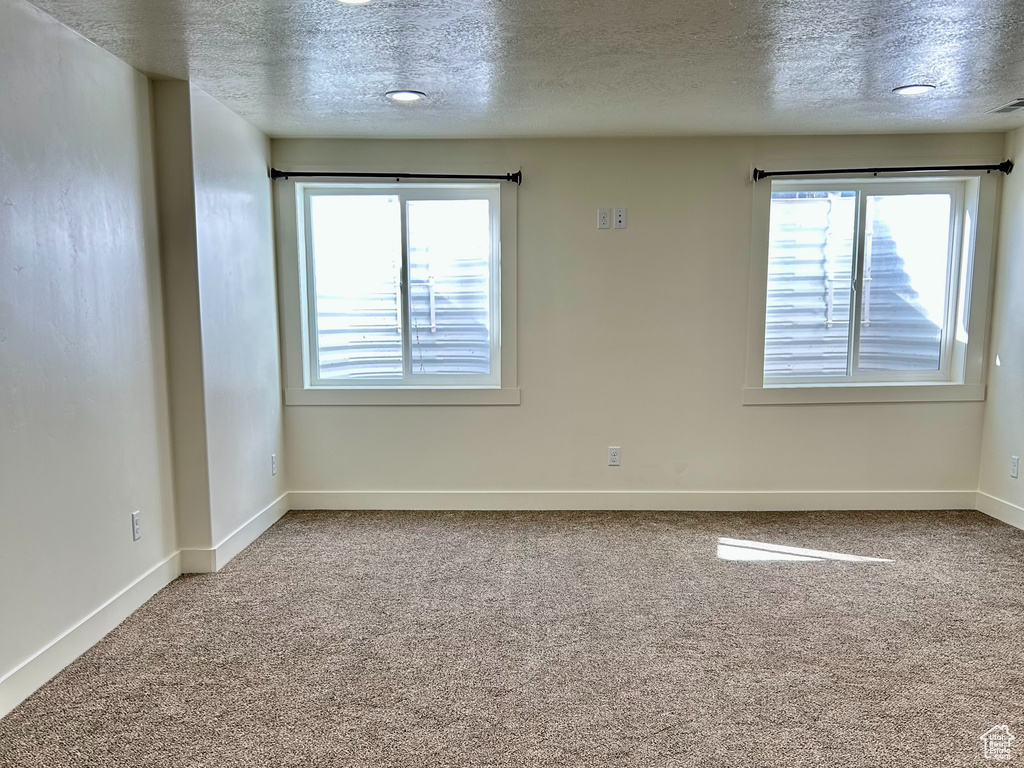 Carpeted spare room featuring a textured ceiling and baseboards