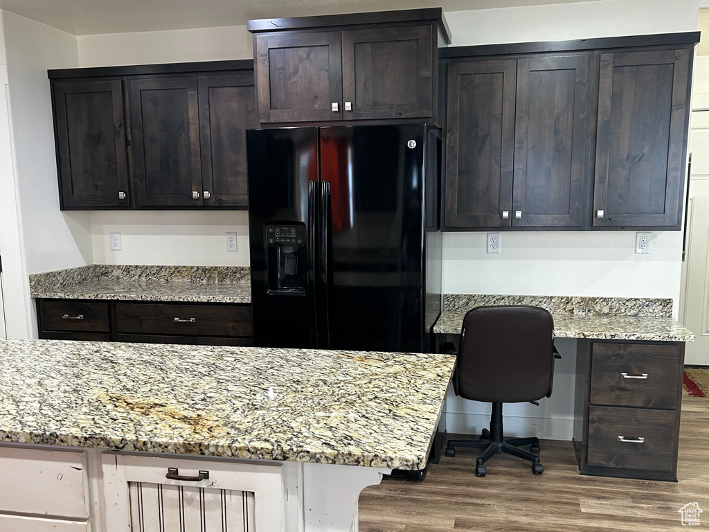 Kitchen with light stone counters, built in desk, wood finished floors, and black fridge