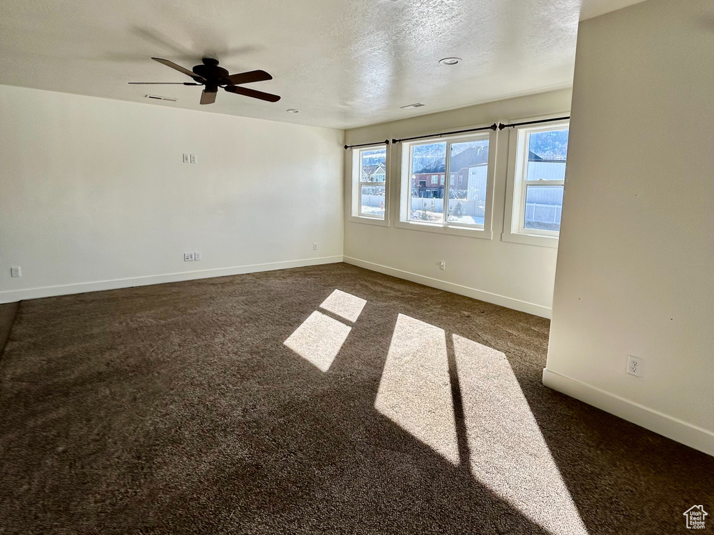 Unfurnished room with a ceiling fan, baseboards, dark carpet, and a textured ceiling