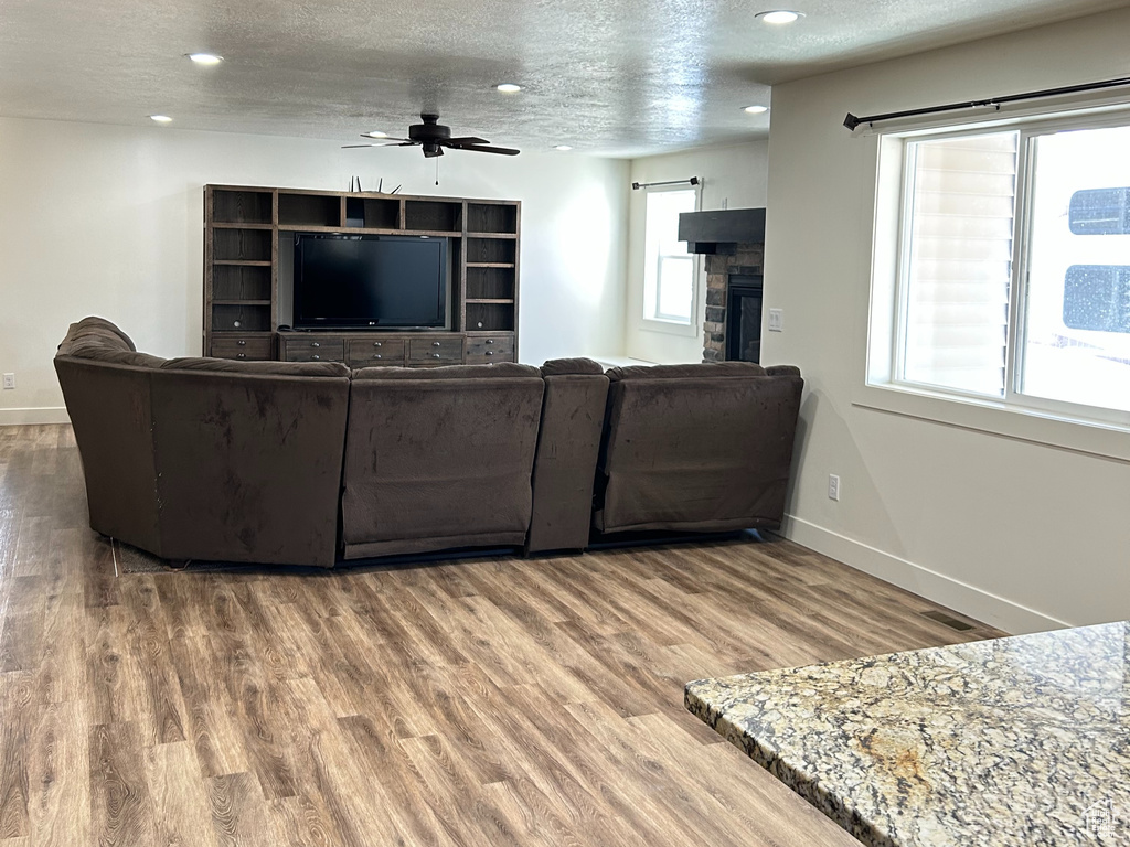 Living room with a ceiling fan, a textured ceiling, wood finished floors, a fireplace, and baseboards