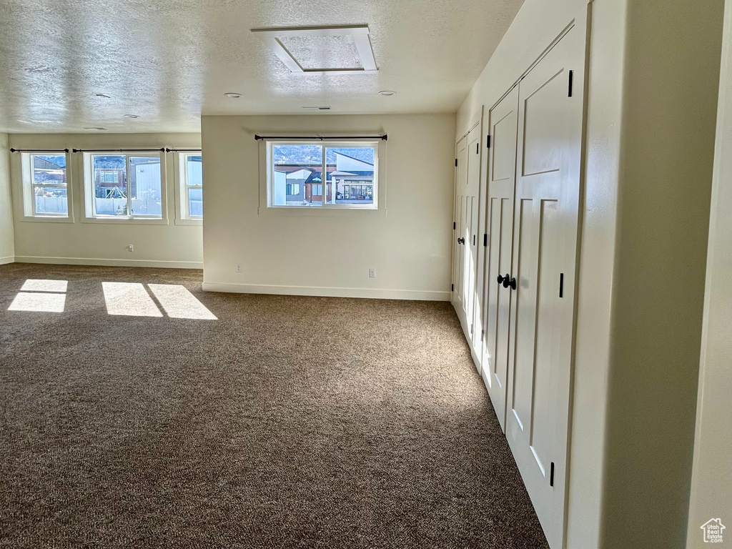 Carpeted empty room with a textured ceiling and baseboards
