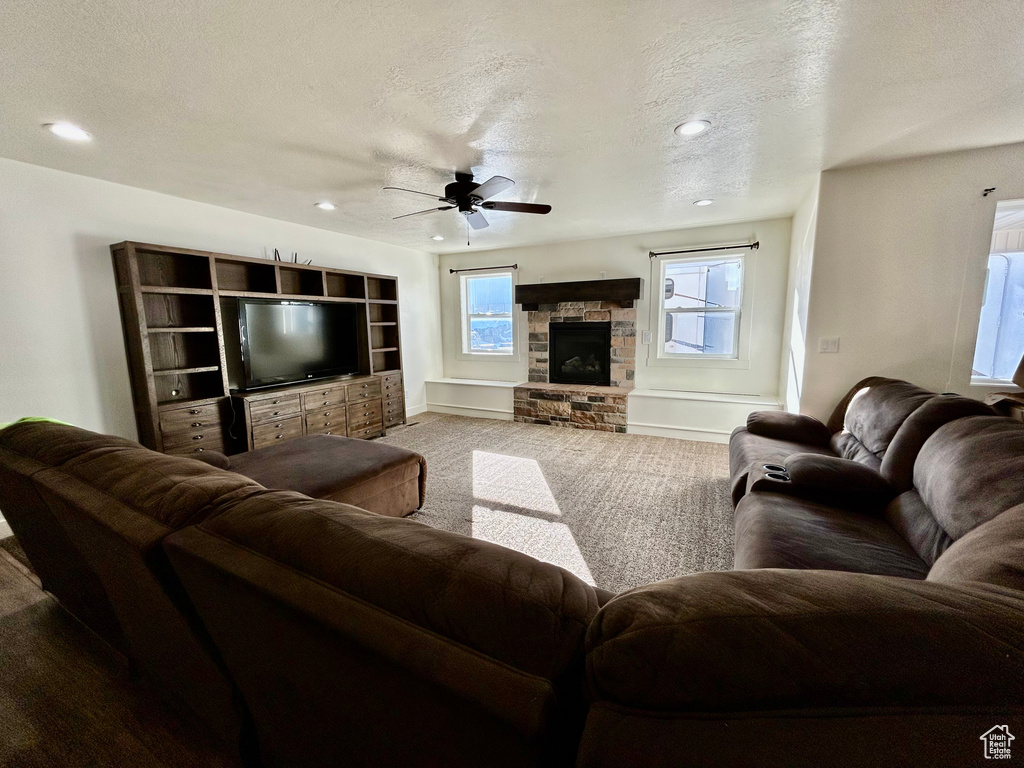 Carpeted living area with a ceiling fan, baseboards, recessed lighting, a stone fireplace, and a textured ceiling