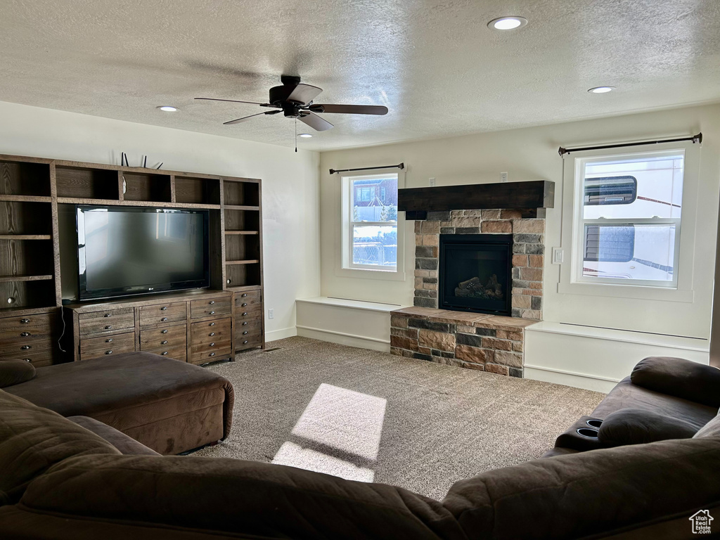 Living room with a ceiling fan, carpet, baseboards, a fireplace, and a textured ceiling