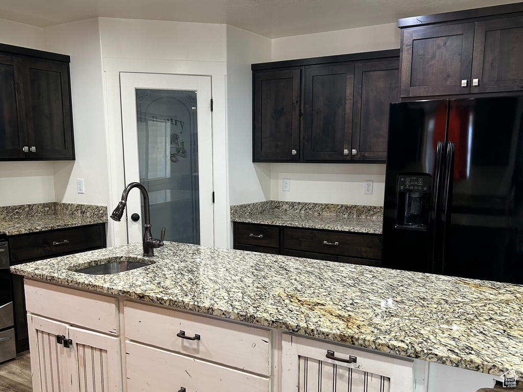 Kitchen with light stone countertops, wood finished floors, black fridge with ice dispenser, a textured ceiling, and a sink