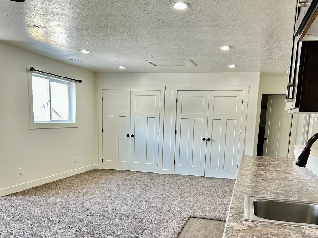 Kitchen with a sink, a textured ceiling, recessed lighting, carpet flooring, and baseboards