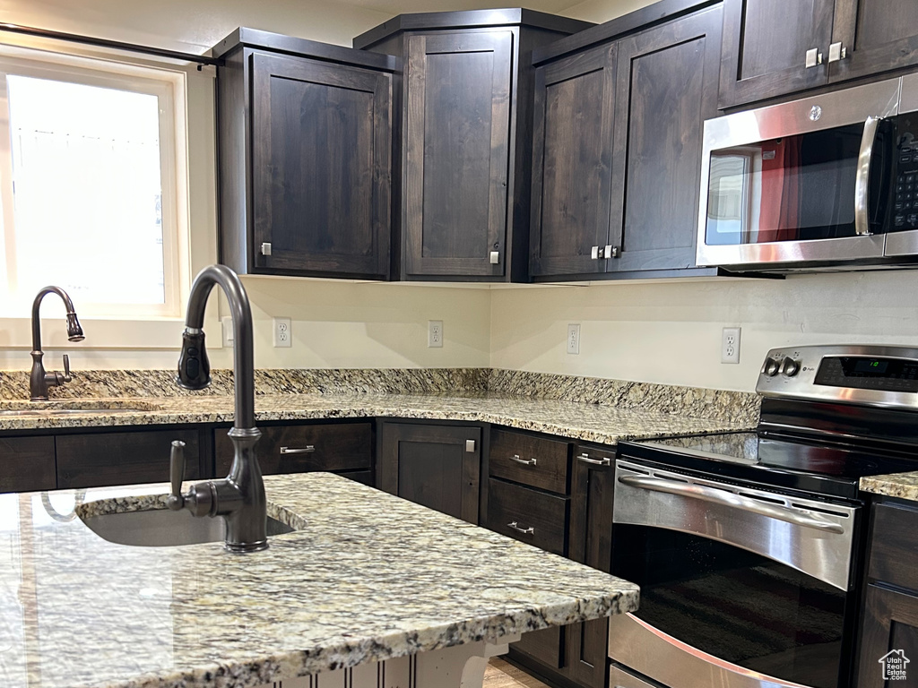 Kitchen with light stone counters, stainless steel appliances, light wood-type flooring, and a sink