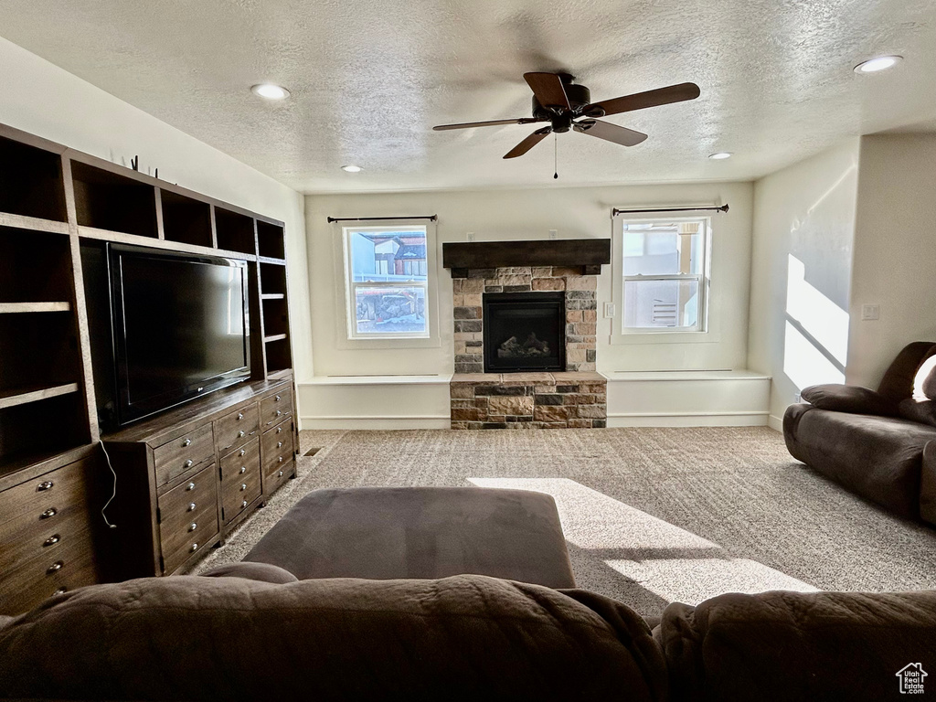 Carpeted living area with a textured ceiling, plenty of natural light, a fireplace, and ceiling fan
