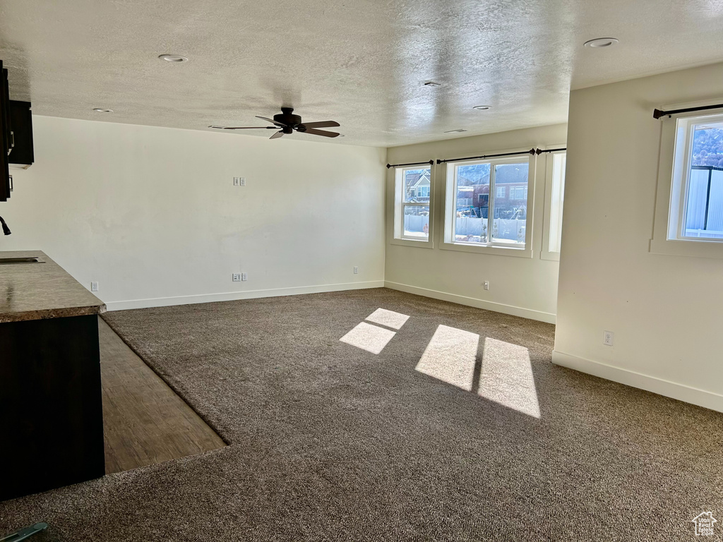 Unfurnished living room featuring a healthy amount of sunlight, carpet, and ceiling fan