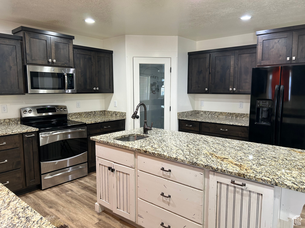 Kitchen with light stone countertops, light wood finished floors, a sink, appliances with stainless steel finishes, and a textured ceiling
