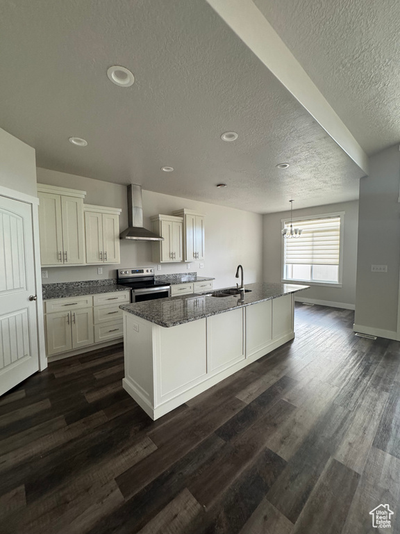 Kitchen with dark wood-type flooring, wall chimney exhaust hood, electric stove, and an island with sink