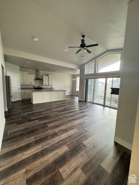 Unfurnished living room featuring dark wood finished floors, ceiling fan with notable chandelier, baseboards, and vaulted ceiling